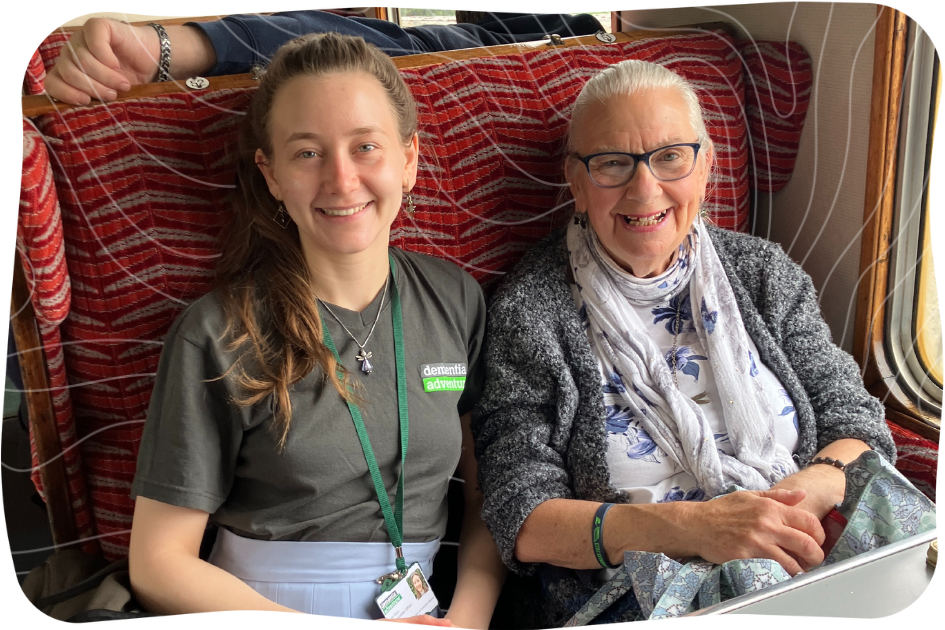 Two women sat side by side on a steam train, smiling at the camera.